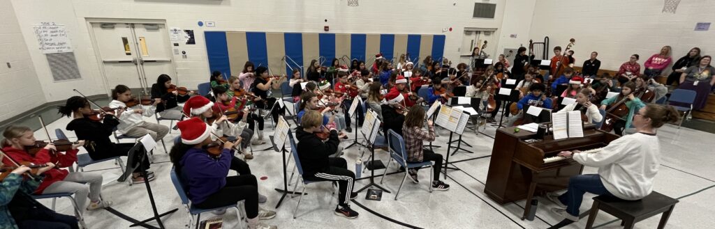 Tharp Orchestra performance in the Tharp gymnasium, some students wearing Santa hats for the holidays.